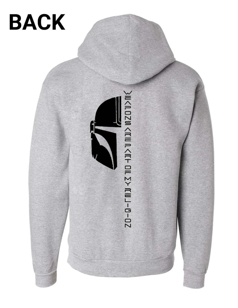 Puede incluir: Sudadera con capucha gris con un gr&aacute;fico de casco mandaloriano negro y el texto "Weapons are part of my religion" impreso verticalmente en la espalda.