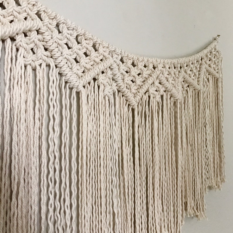 May include: A white macrame wall hanging with a geometric pattern and long fringe.
