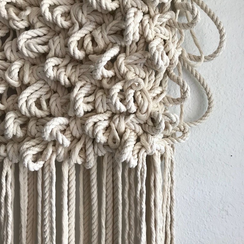 May include: A beige macrame wall hanging with a textured, knotted design and a fringe of tassels.