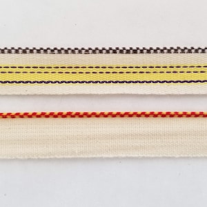 May include: Two pieces of white fabric trim with different colored stitching. The top trim has a yellow stripe with a black line on either side. The bottom trim has red stitching.