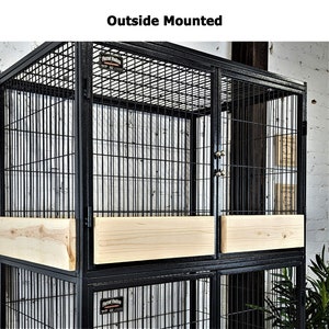 May include: A black metal bird cage with a rectangular shape and a wire mesh design. The cage features wooden panels and the text "Outside Mounted". The cage is designed for parrots.