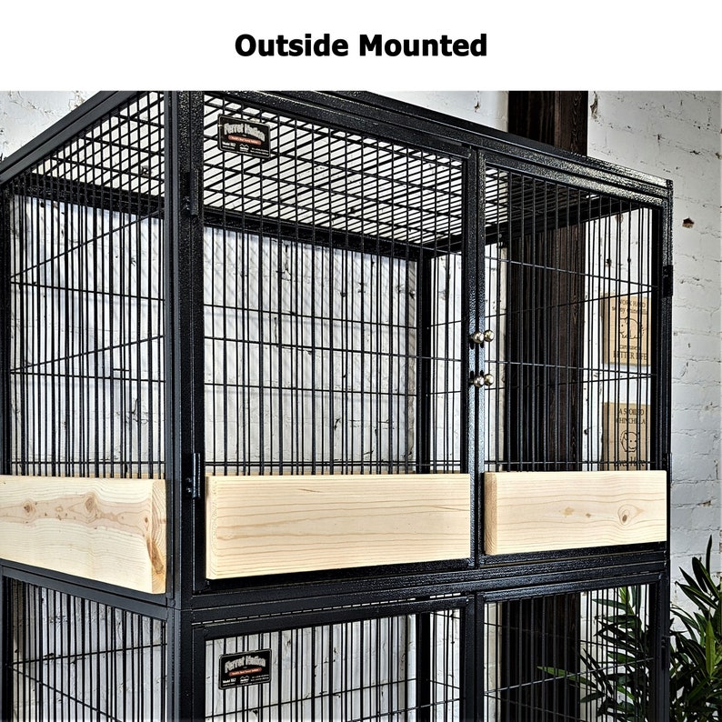 May include: A black metal bird cage with a rectangular shape and a wire mesh design. The cage features wooden panels and the text "Outside Mounted". The cage is designed for parrots.