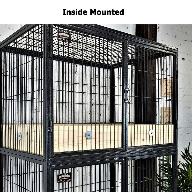 May include: Black metal pet cage with wire mesh sides and doors. The cage has a wooden base and the text "Inside Mounted" at the top. The cage is designed for indoor use.