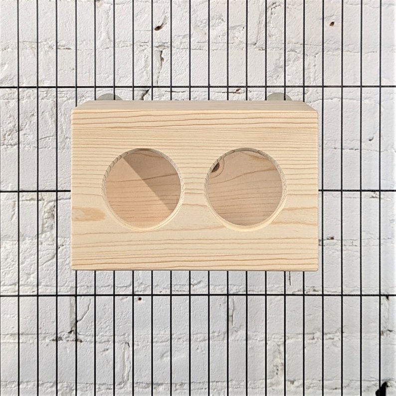 May include: A wooden feeder with two round openings for small animals. The feeder is made of natural wood and is designed to be hung inside a cage.
