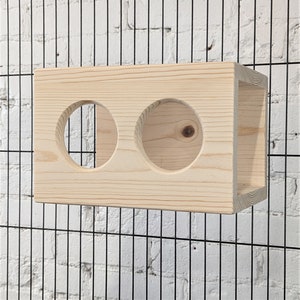 May include: A wooden box with two circular openings, designed for small animals to play and explore. The box is made of natural wood and has a light brown color.
