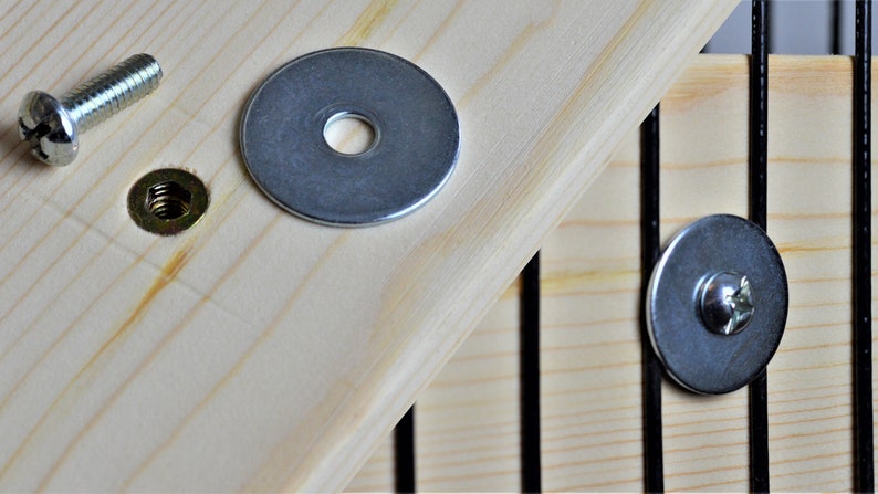May include: Close-up of hardware components, including a silver screw, a nut, and a washer, arranged on a light-coloured wooden surface. The components are for assembly or repair, likely for furniture or a similar project.