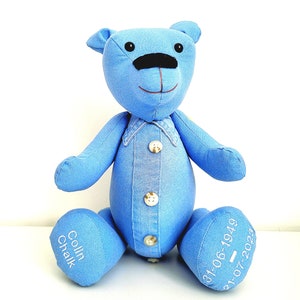 May include: Blue denim teddy bear with a button-up shirt and embroidered details. The bear's feet are embroidered with the name "Colin Chalk" and the dates "31-06-1949" and "31-07-2023".