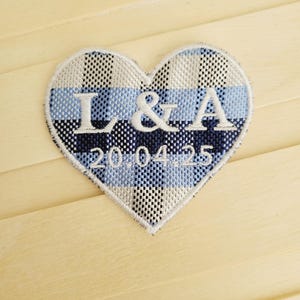 May include: A blue and white checked heart-shaped patch with the initials "L & A" and the date "20.04.25" embroidered in white.