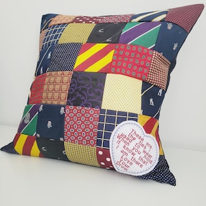 May include: A square cushion made from a patchwork of colourful ties. The cushion has a heart-shaped patch with the text "These are the ties used to wear when you hold it know that I am there Love Your Drew".
