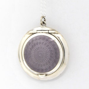 May include: A silver locket necklace with a hinged lid and a purple enamel design. The locket is circular and has a delicate chain.