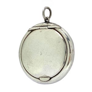 May include: A silver-coloured, round locket pendant with a hinged opening. The locket has a smooth, polished surface and a small loop at the top for a chain. The pendant is designed to hold a small photograph or keepsake.