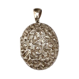 May include: An oval-shaped silver-toned metal locket pendant featuring an intricate, raised floral and leaf relief pattern across its entire front surface. The pendant includes a polished, smooth metal bail at the top for attachment to a chain.