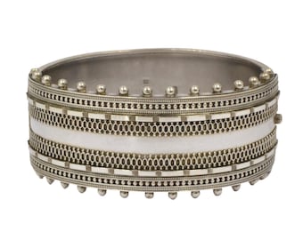 May include: A silver bangle bracelet with a white enamel band and intricate geometric designs. The bracelet has a hinged closure.