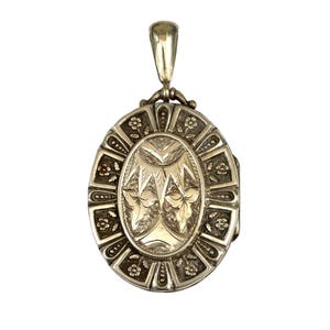 Peut inclure: Un pendentif médaillon ovale en métal argenté présentant un motif floral gravé complexe sur la bordure extérieure et un panneau ovale central avec un motif de feuilles détaillé. La pièce comprend une bélière polie sur le dessus.