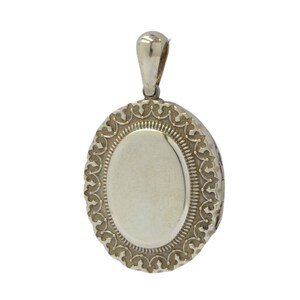 Op de afbeelding: Zilveren ovaal medaillon met een delicaat, versierd ontwerp rond de rand. Het medaillon heeft een scharnierend deksel en een lus om een ​​ketting aan te bevestigen.