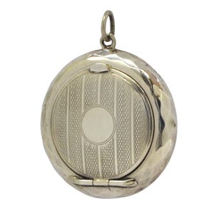 May include: A silver locket with a hinged lid and a decorative engraved design. The locket is round and has a smooth, polished finish.
