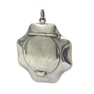 May include: A silver-toned metal locket pendant with a six-pointed star shape and a smooth, circular centre panel. The pendant features a hinged top section and a small metal loop at the very top for attachment to a chain or cord.