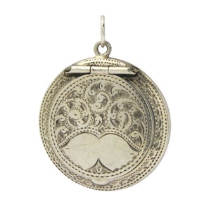 May include: Silver locket pendant with a hinged lid and an engraved floral design. The locket has a heart-shaped opening on the front.