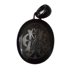 May include: Black oval locket with a carved design of intertwined initials. The locket has a black metal bail.