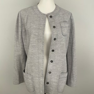 May include: A light gray jacket with a round neckline and a button-up front. The jacket has two front pockets and decorative stitching. The buttons are dark gray. The jacket is displayed on a mannequin.