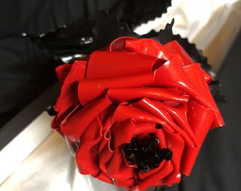 May include: A red metal rose with black metal leaves. The rose is in a white box with a black lining.