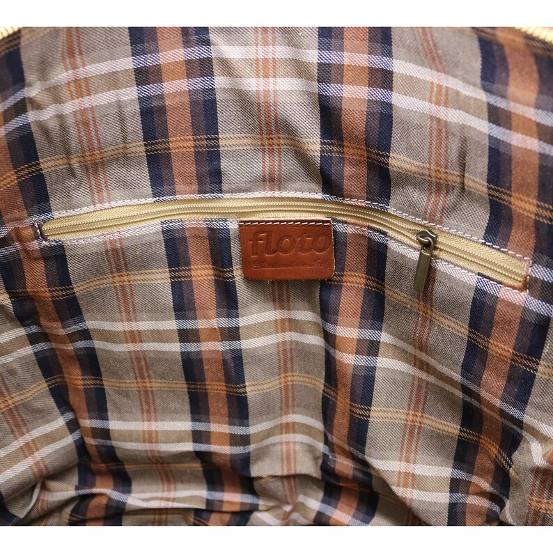 May include: Interior of a bag with a plaid pattern in shades of brown, tan, and navy blue. A gold zipper runs across the top, and a brown leather tag with the word "floto" is sewn inside.