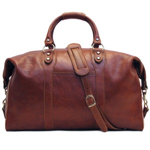 May include: A brown leather duffel bag with a top handle and a detachable shoulder strap. The bag has a rectangular shape with a zipper closure and metal hardware. The bag is made of a smooth, polished leather.