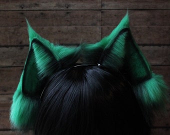 May include: Green furry cat ears headband. The headband is worn on a black wig with bangs.