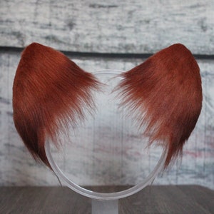 May include: A pair of reddish-brown faux fur cat ears on a clear plastic headband.