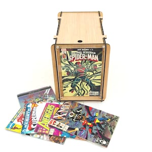 May include: A wooden comic book display case with a clear front panel, showcasing a Spider-Man comic book. Several other comic books are fanned out below. The case is made of light-colored wood with black accents.