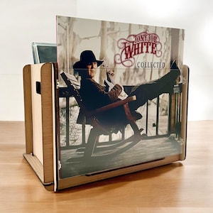 May include: A wooden vinyl record holder with a clear acrylic front panel. The front panel displays the album cover of "Tony Joe White Collected." The album cover features a man in a rocking chair. The holder is on a wooden surface.