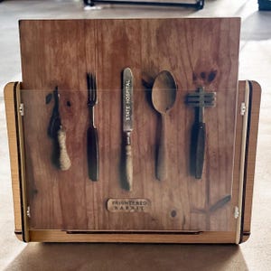 Op de afbeelding: Houten display case met een helder voorpaneel, met vintage keukengerei tegen een achtergrond met houtnerf. Het mes is voorzien van het opschrift "STATE HOSPITAL" en de onderkant luidt "FRIGHTENED RABBIT". De behuizing heeft een licht houten frame.
