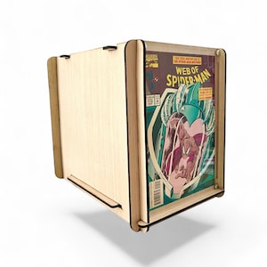 May include: A wooden comic book display case with a clear front panel. The case holds a comic book with the title "Web of Spider-Man" and a colorful illustration of Spider-Man. The case is made of light-colored wood.