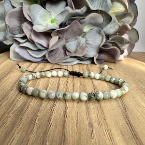 May include: A green and white beaded bracelet with a black cord and adjustable knot closure.