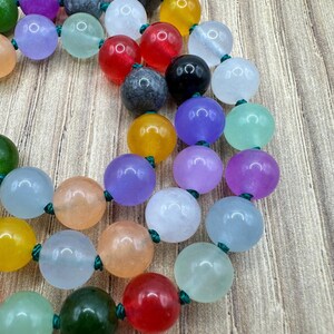May include: A colourful beaded necklace with round, smooth beads in various shades of green, blue, purple, red, yellow, and white. The beads are strung on a green cord.