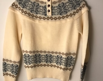 May include: A cream-colored knitted sweater with a brown and gray geometric pattern. The sweater has a mock neck and a single button closure.