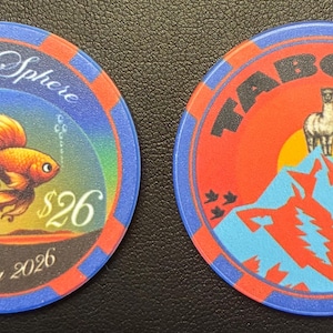 May include: Two circular coasters. One features a goldfish illustration with the text "Live @ Sphere" and "Spring 2026". The other coaster has an illustration of a llama on a mountain with the word "TABOOT". Both have blue and red accents.