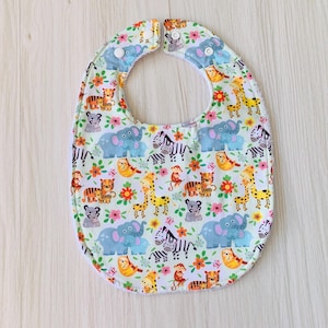 May include: A white baby bib with a colorful print of animals, including elephants, zebras, tigers, and monkeys. The bib has a rounded shape and is made of soft fabric.