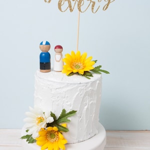 May include: A white wedding cake decorated with flowers and a topper that says "best day ever".
