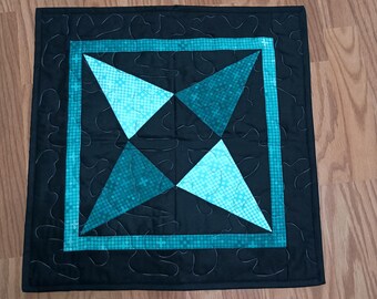 May include: A black quilted square pillow with a teal and blue geometric design in the center.