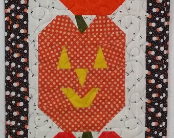 Pode incluir: Três abóboras de tecido laranja e amarelo com rostos de jack-o'-lantern, dispostas verticalmente sobre um fundo branco com uma borda de bolinhas pretas e brancas.