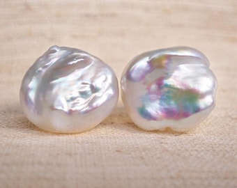 May include: Two white baroque pearls with an irregular, organic shape and a high-luster finish. The surface of each pearl displays a subtle iridescent sheen with hints of pink, blue, and green reflections across their textured, bumpy surfaces.