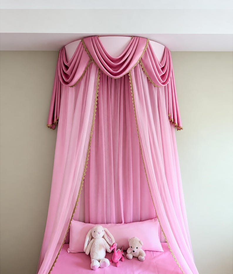 May include: A pink bed canopy featuring draped fabric with gold trim, suspended from a circular mount. Below the canopy, a pink pillow and pink bedding are arranged with a plush rabbit, a small pink dinosaur, and a small plush bear toy.