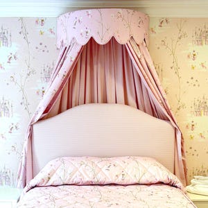Könnte beinhalten: Ein rosa Himmelbett mit einem weißen und rosa karierten Kopfteil und einer rosa und weißen, floral gemusterten Bettdecke.