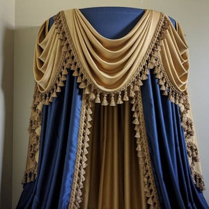 Könnte beinhalten: Ein Paar blaue und goldene Vorhänge mit Quasten. Die Vorhänge sind über einen Bettrahmen drapiert und haben eine dekorative Gardine.