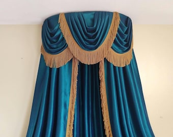 May include: A deep teal curtain set featuring a draped valance with gold fringe trim. The fabric has a smooth, satin-like finish with vertical folds. The valance is layered with a scalloped edge, and the vertical panels are edged in gold fringe.
