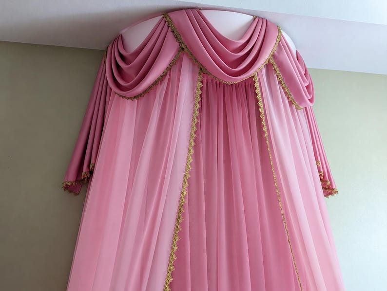 May include: A pink bed canopy featuring a semi-circular top mount with draped fabric swags. The canopy includes sheer pink curtains and opaque pink side panels, all accented with decorative gold lace trim along the edges and the valance.