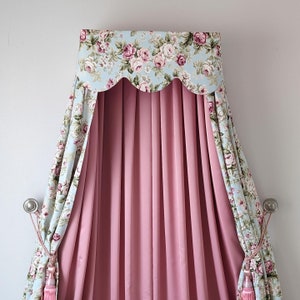 May include: A canopy bed with a pink and white floral patterned canopy. The canopy is made of a soft, flowing fabric and has a scalloped edge. The bed is draped with a pink curtain.