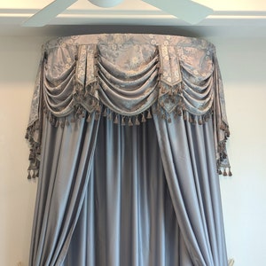 Könnte beinhalten: Ein grauer und weiß gemusterter Baldachin-Bettvorhang mit Quasten. Der Vorhang ist aus einem weichen, fließenden Stoff gefertigt und soll eine gemütliche und elegante Atmosphäre im Schlafzimmer schaffen.