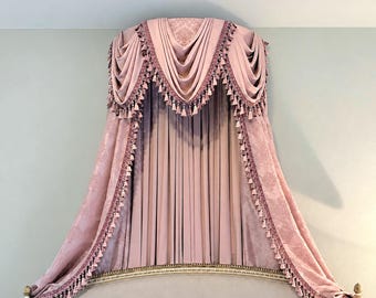 May include: A dusty pink bed canopy featuring a draped valance with intricate damask patterns and decorative fringe trim. The fabric hangs in soft, vertical folds, creating a layered effect over the headboard of a bed frame.